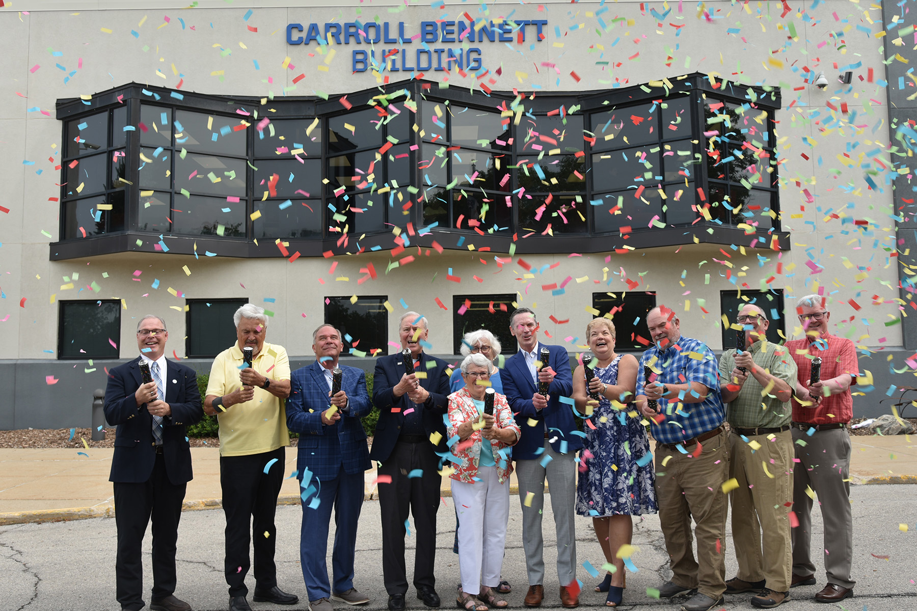 DMACC administrators and members of the Bennett family celebrate the dedication and renaming of the DMACC Newton Campus as the Carroll Bennett Building by shooting confetti into the air.
