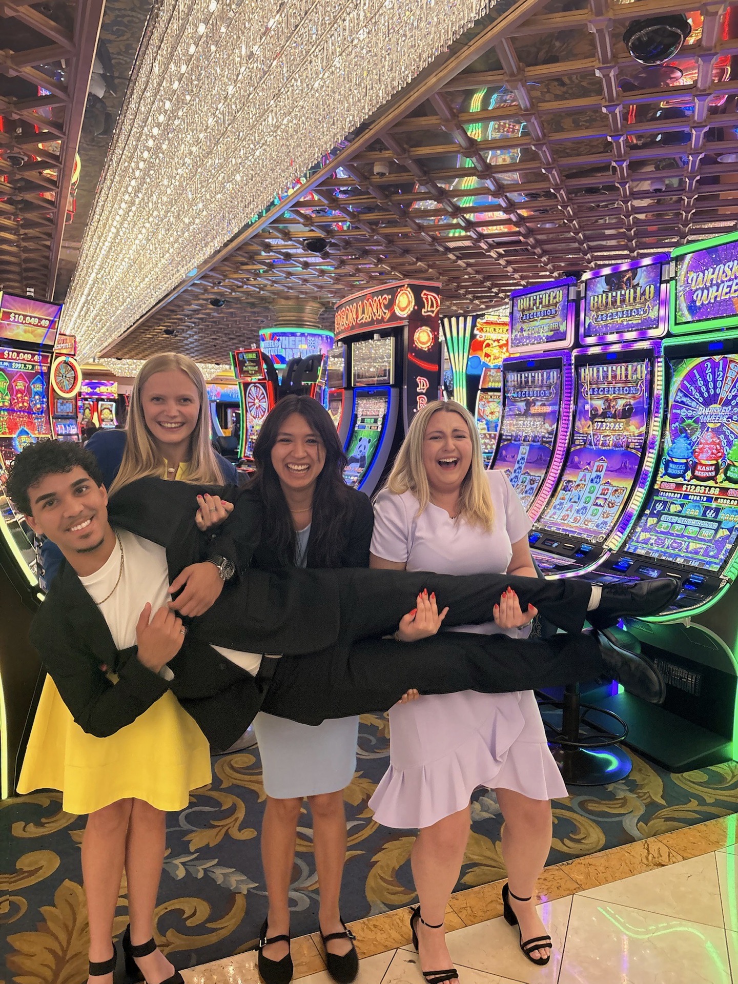FBLA students in Las Vegas Three people carry a person horizontally posing for a photo in front of bright lights and slot machines