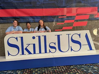 Three students stand in front of Skills USA large block letters