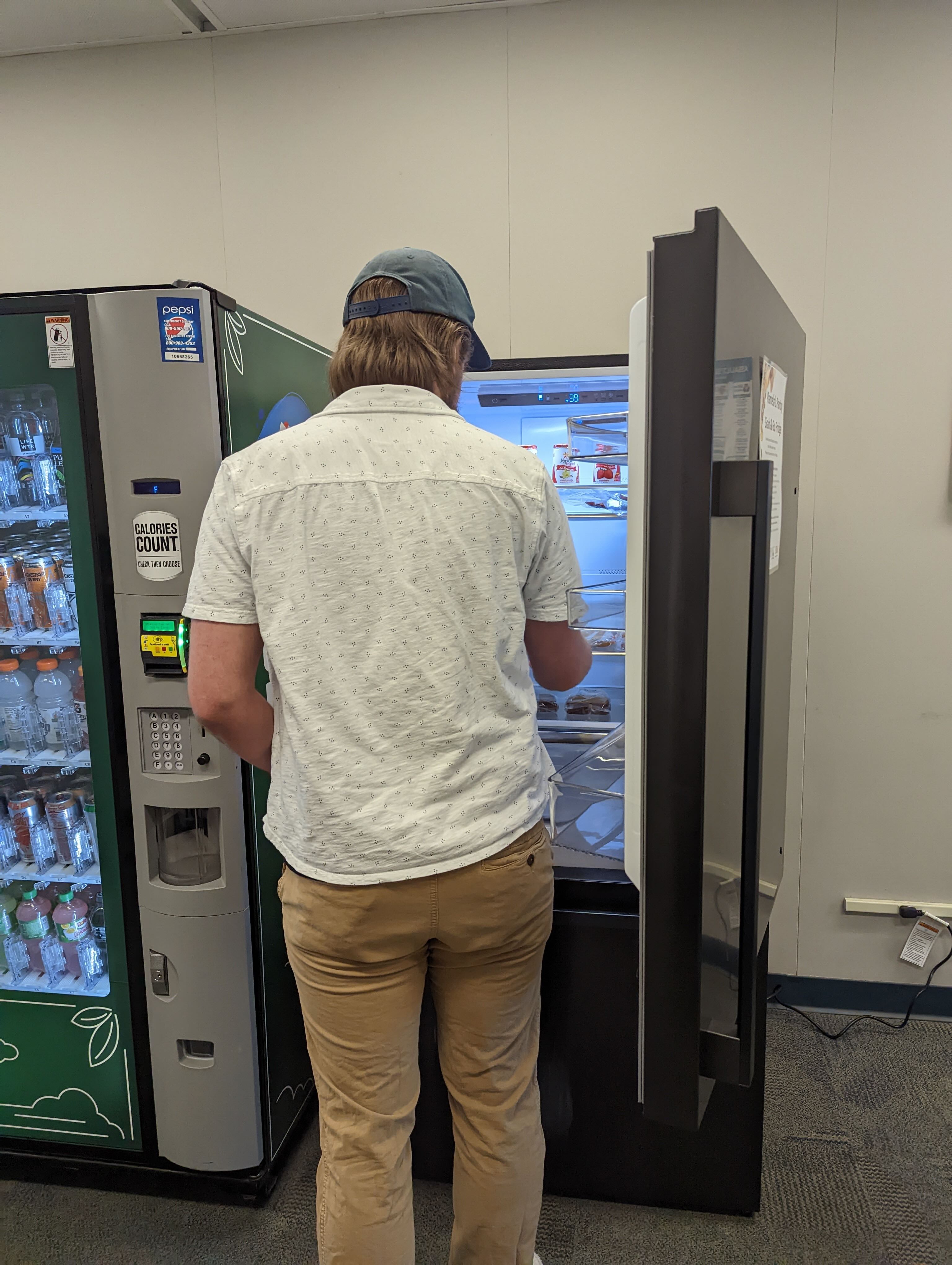 A person in a white collared shirt and khaki pants stands in front of an open fridge with their backed turned.