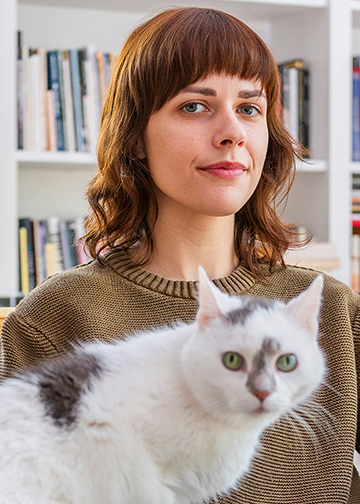Headshot photo of writer and professor Paige Lewis, red wavy hair with blunt bangs, pictured with a white cat with gray spots.